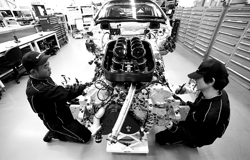 Two mechanics install exhaust manifolds along both sides of the engine with skilled precision